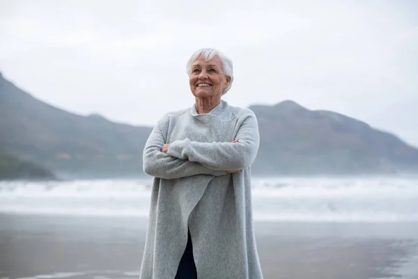 Starší žena stojící s rukama zkříženýma na pláži — Stock fotografie