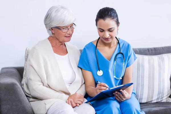 Doctor and senior woman discussing on clipboard — Stock Photo, Image