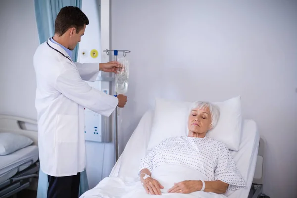 Doctor adjusting iv drip while patient lying on bed — Stock Photo, Image