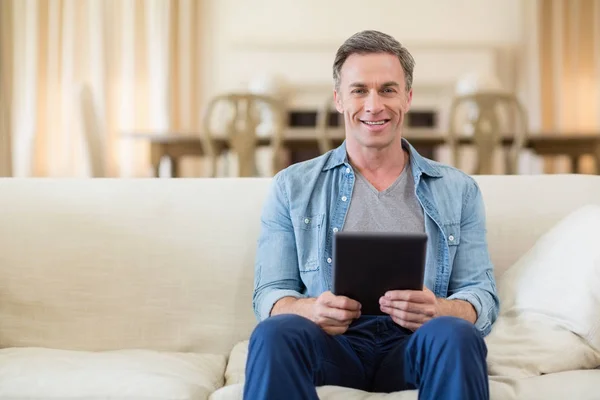 Retrato del hombre sentado en el sofá y utilizando la tableta digital en la sala de estar — Foto de Stock