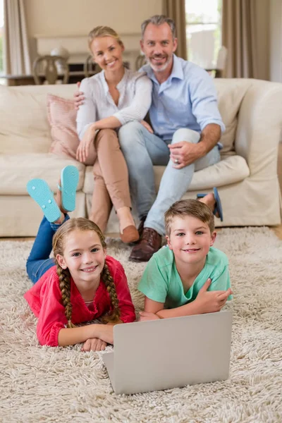 Porträtt av syskon liggande på matta medan föräldrar sitter i bakgrunden — Stockfoto