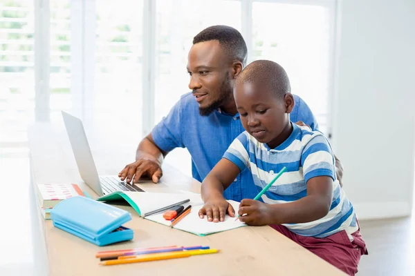 Father using laptop and son doing his homework in living room — Stock Photo, Image
