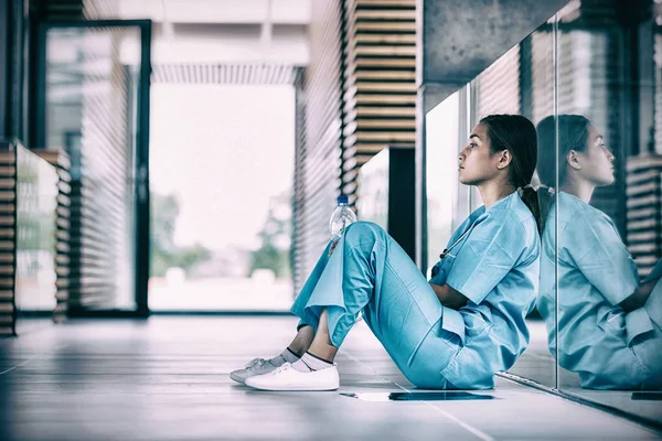 Zijaanzicht van verpleegkundige zittend op de vloer — Stockfoto