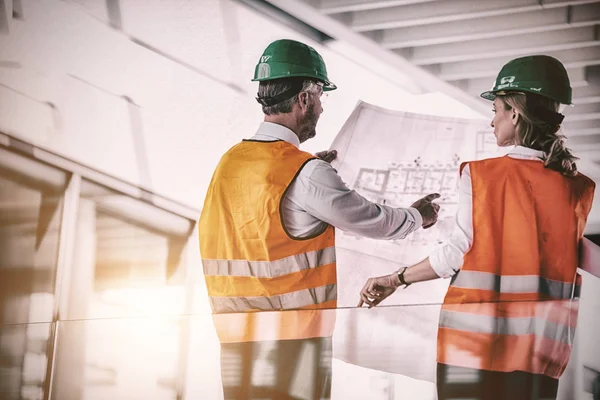 Arquitectos discutiendo con planos en pasillo de oficinas —  Fotos de Stock