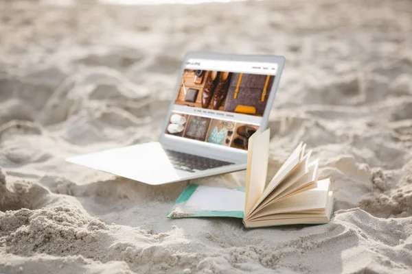 Öppna boken och laptop på sanden på stranden — Stockfoto