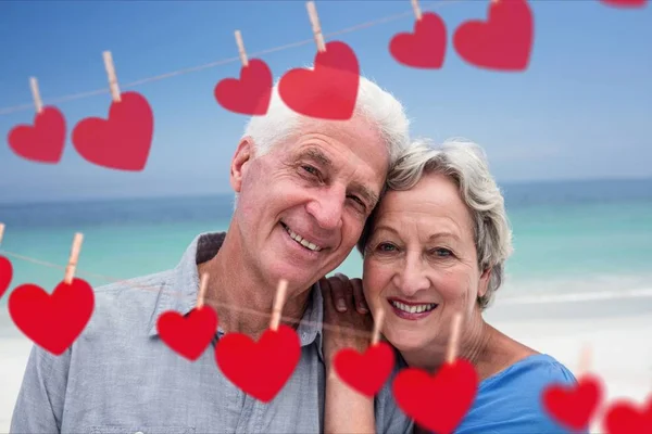 Retrato de la persona mayor abrazándose en la playa contra los corazones colgando de una línea — Foto de Stock