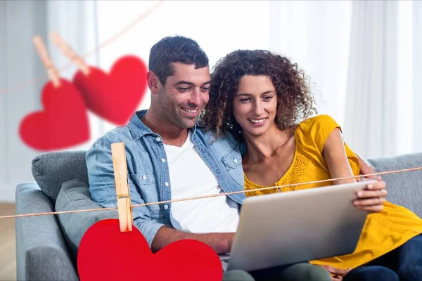 Hanging red hearts and couple using a laptop — Stock Photo, Image