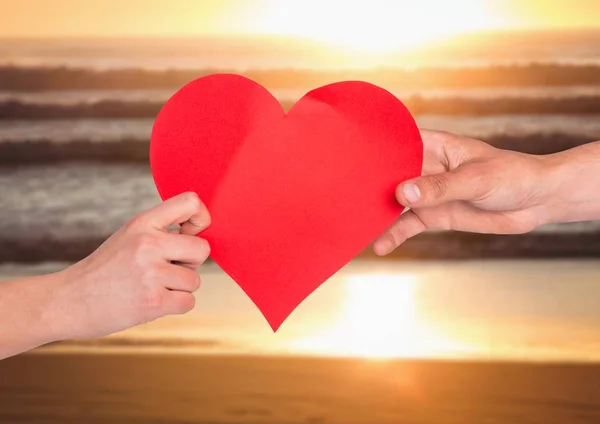 Mãos de casal segurando coração vermelho na praia — Fotografia de Stock