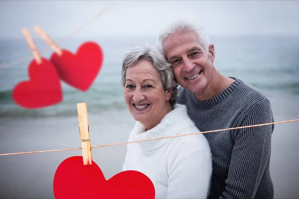 Cuori appesi e coppia anziana che si abbraccia sulla spiaggia — Foto Stock