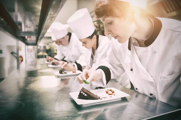 Chefs de pé em uma fileira de pratos de sobremesa de enfeite — Fotografia de Stock