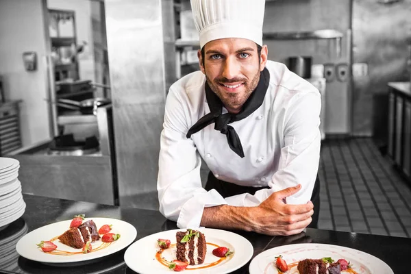 Glada kocken tittar kameran bakom disken desserter — Stockfoto