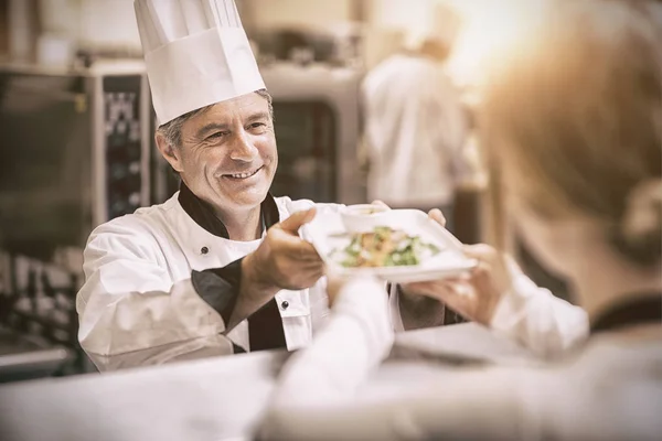 Chef handing dinner dish to waitress at order station — Stock Photo, Image