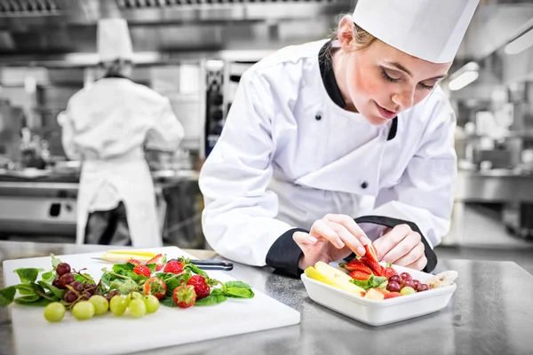 Female chef putting a strawberry in the fruit salad — Stock Photo, Image