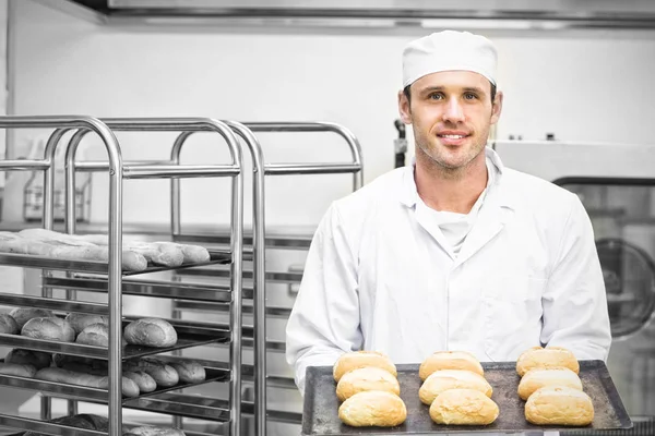 Feliz panadero joven sosteniendo algunos rollos en una bandeja para hornear — Foto de Stock
