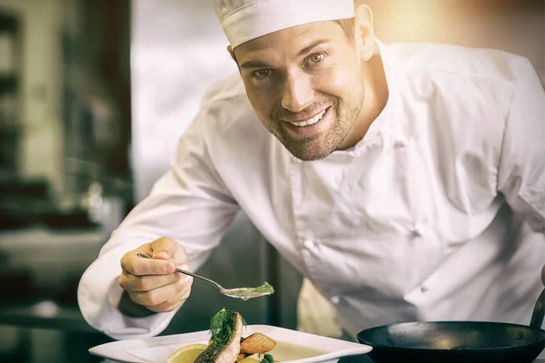 Chef masculino sonriente adornando comida en la cocina — Foto de Stock