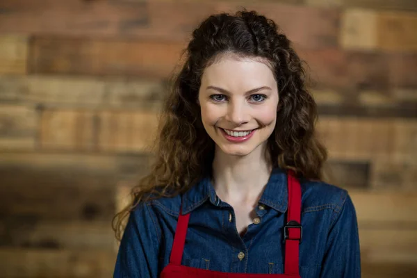 Portret van lachende serveerster permanent tegen houten muur — Stockfoto