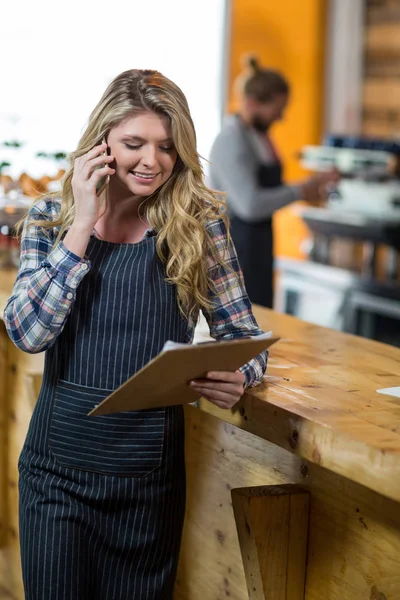 Офіціантка дивиться на буфер обміну під час розмови на мобільному телефоні в кафе — стокове фото