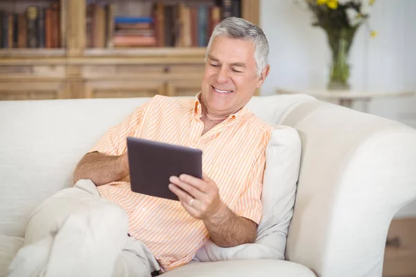 Sorrindo homem sênior usando tablet digital na sala de estar — Fotografia de Stock