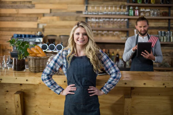 Portret van lachende serveerster permanent met handen op heup aan balie — Stockfoto