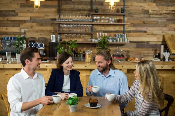 Amigos felizes interagindo uns com os outros enquanto tomam café — Fotografia de Stock