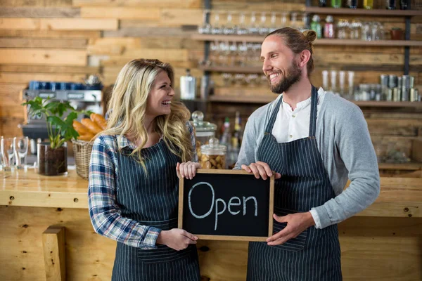 Servitris och servitör som står med öppna tecken styrelsen i café — Stockfoto