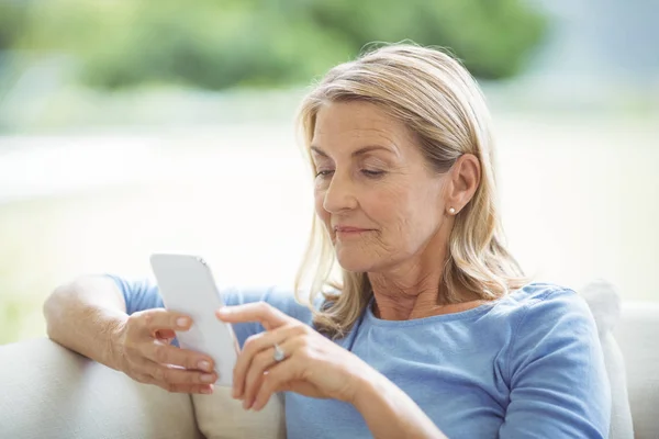 Oudere vrouw die mobiele telefoon gebruikt in de woonkamer — Stockfoto