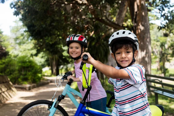 Retrato de niños sonrientes de pie con bicicleta en el parque —  Fotos de Stock