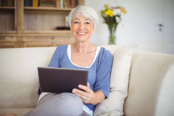 Mujer mayor sonriente usando tableta digital en la sala de estar —  Fotos de Stock