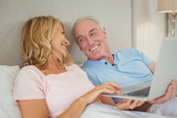 Feliz pareja de ancianos en la cama usando el ordenador portátil —  Fotos de Stock