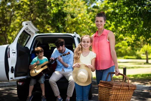 Portrait de mère et fille debout avec panier pique-nique tandis que père et fils jouant de la guitare en b — Photo