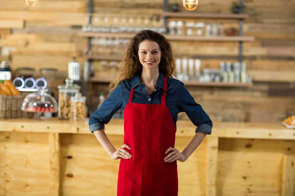 Portret uśmiechający się kelnerka stojąc z ręce na biodra w kasie — Zdjęcie stockowe