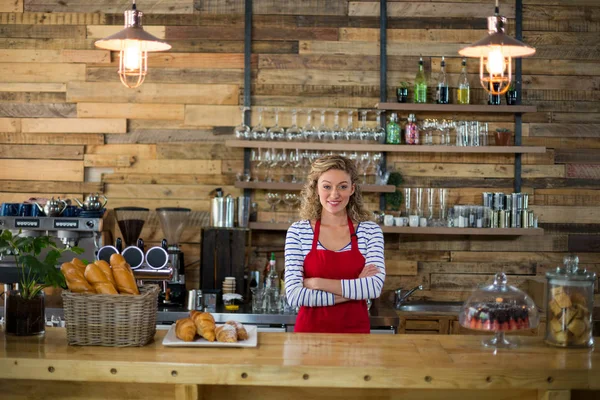 Porträtt av leende servitris som står med armarna korsade vid counter — Stockfoto