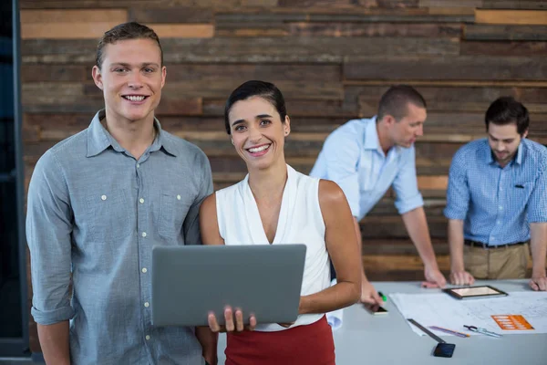 Glimlachende zakenmensen permanent in kantoor met laptop — Stockfoto