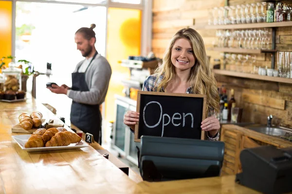 Ler servitris som står vid counter och visar skiffer med öppen skylt — Stockfoto