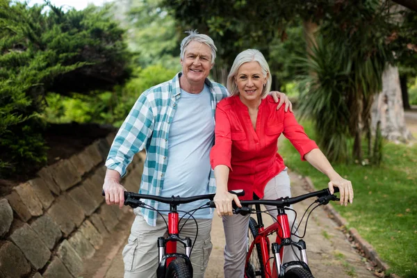 Портрет старшої пари, що стоїть з велосипедом у парку — стокове фото