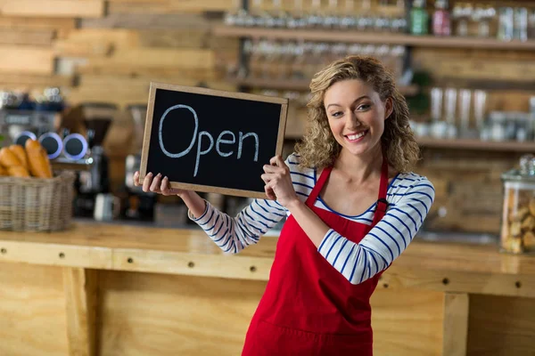 Cameriera sorridente in piedi con cartello aperto nel caffè — Foto Stock