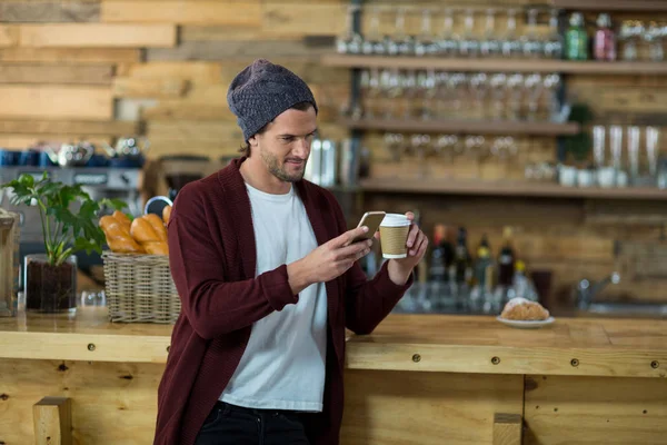 Człowiek przy użyciu telefonu komórkowego przy filiżance kawy w kasie — Zdjęcie stockowe