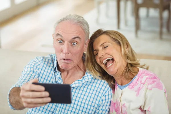 Pareja mayor tomando una selfie en el teléfono móvil en la sala de estar — Foto de Stock