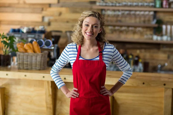 Uśmiechający się kelnerka stojąc z ręce na biodra w kawiarni — Zdjęcie stockowe