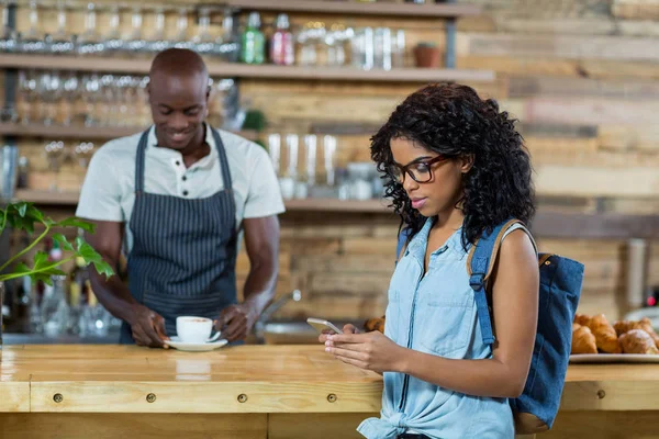 Frau benutzt Handy, während Kellner im Hintergrund steht — Stockfoto