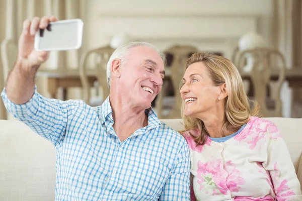 Pareja mayor tomando una selfie en el teléfono móvil en la sala de estar — Foto de Stock