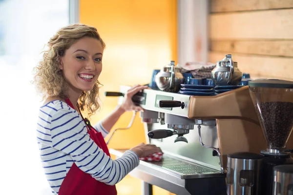 Camarera sonriente limpiando la máquina de café espresso con servilleta en la cafetería —  Fotos de Stock