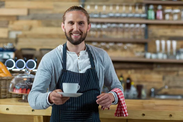 Porträt eines lächelnden Kellners, der eine Tasse Kaffee anbietet — Stockfoto