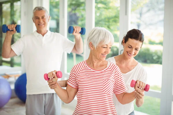 Female trainer assisting senior couple in performing exercise — Stock Photo, Image