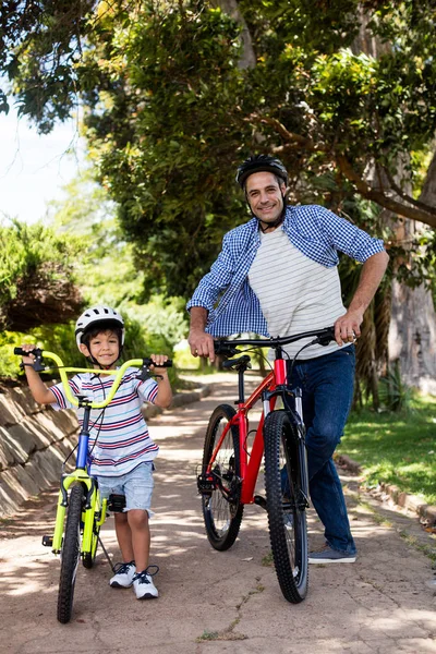 Retrato de pai e filho de pé com bicicleta no parque — Fotografia de Stock