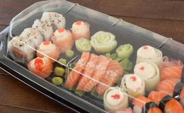 Uppsättning av blandade sushi hålls i en plastlåda på träbord — Stockfoto