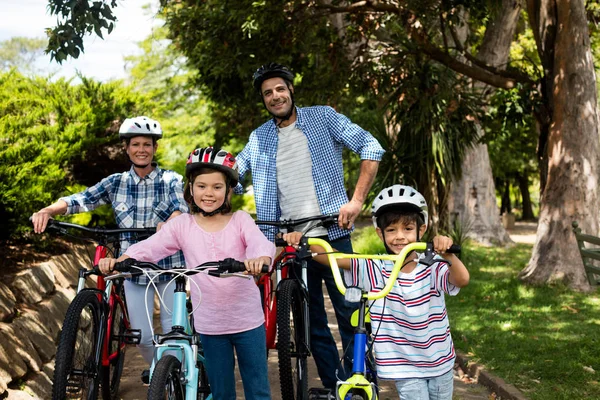 Retrato de padres e hijos de pie con bicicleta en el parque — Foto de Stock