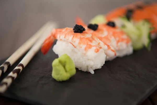 Nigiri sushi servido con palillos en pizarra de piedra negra sobre mesa de madera — Foto de Stock
