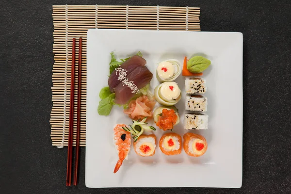 Assortiment de sushis servi avec des baguettes en assiette blanche sur tapis de sushi — Photo