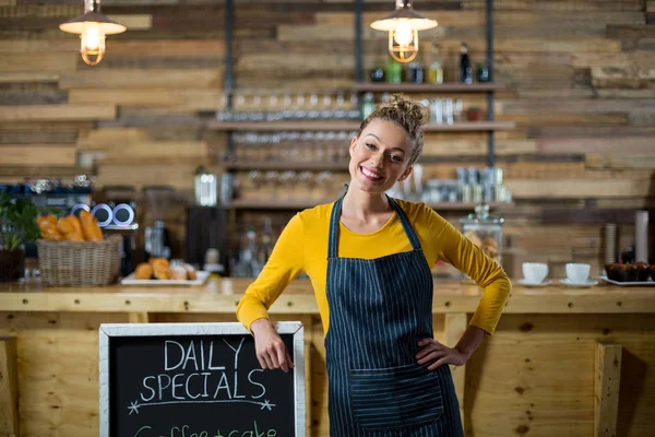 Uśmiechnięta kelnerka, stojąc z menu płyty w kawiarni — Zdjęcie stockowe